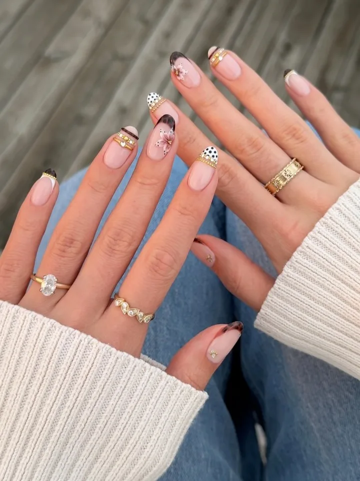 Mixed fall French tips with brown patterns, black polka dots, pink flowers, and gold bead and gem bands