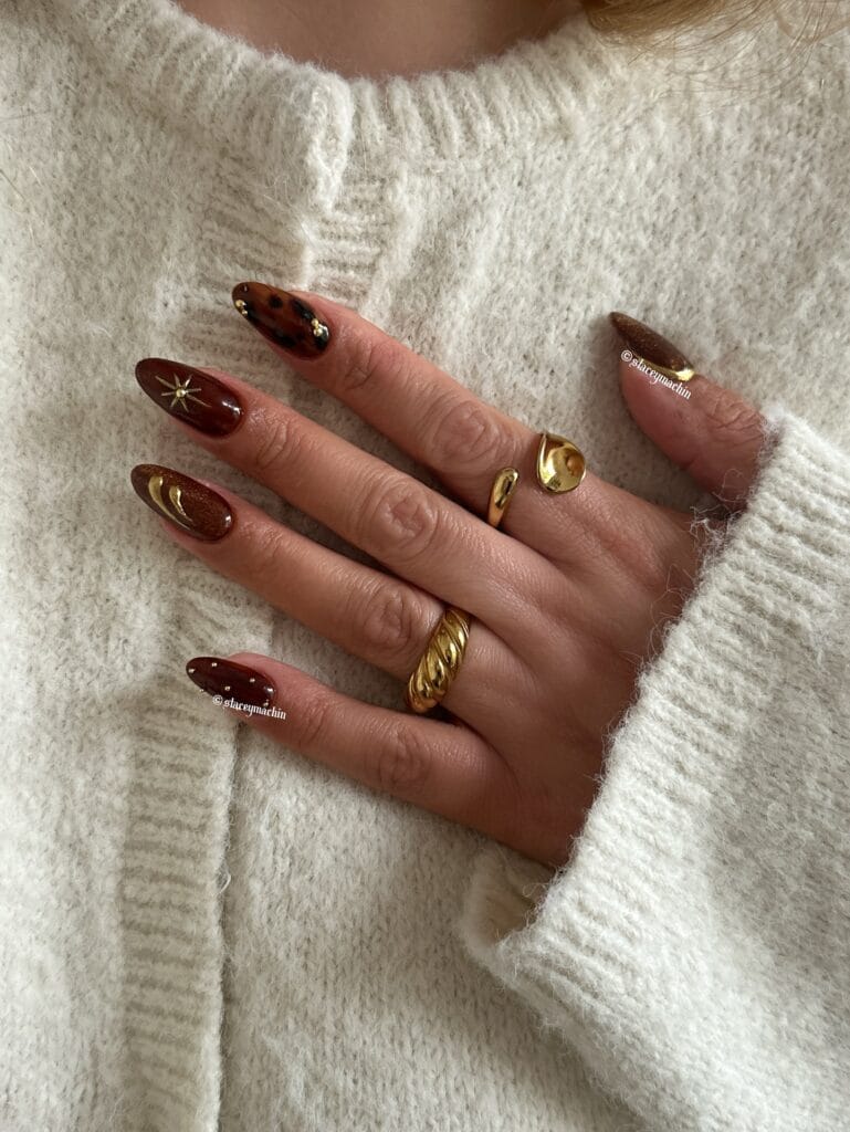 Almond brown fall nails with tortoiseshell, brown jelly polish, gold starburst and crescent studs, and tiny gold dots