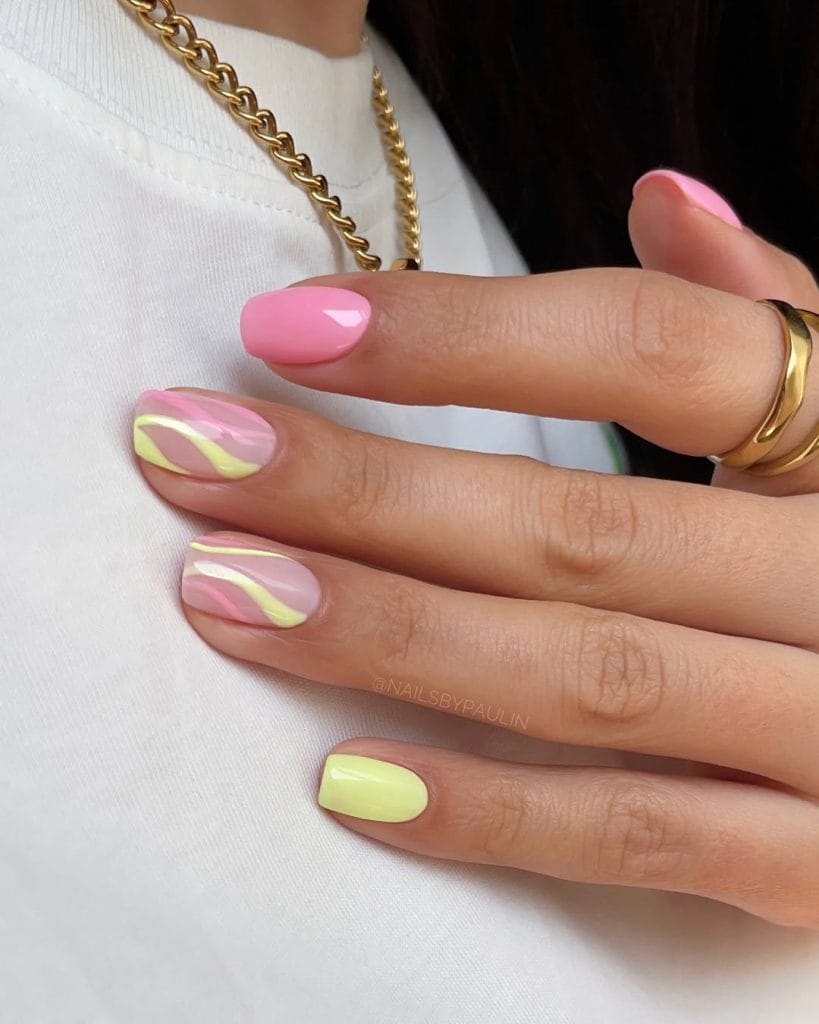 Short oval August nails with solid pink, bright yellow, and pink base with yellow swirl patterns
