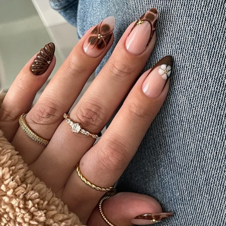 Autumn nails with a 3D chocolate shell, blurred brown flower, brown French tips, a white flower, and gold beads