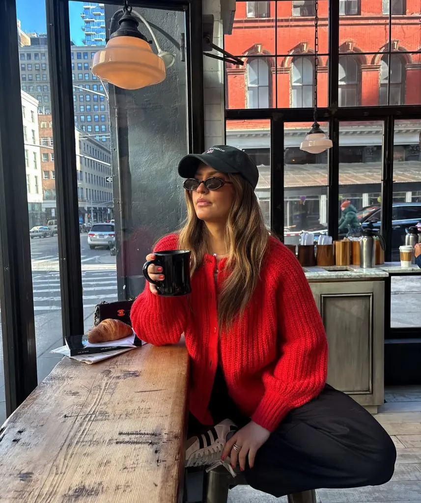 Cozy fall outfit with red chunky knit cardigan over black trousers, styled with black baseball cap and sunglasses