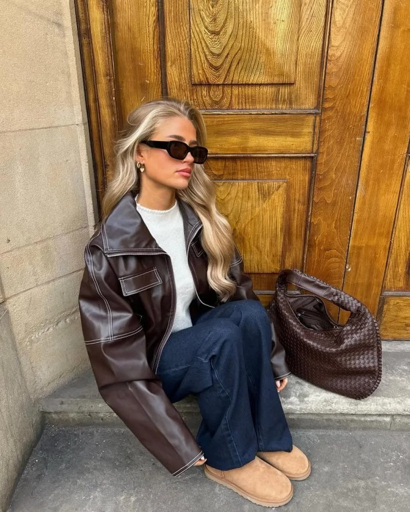Casual fall outfit with brown leather jacket, cream sweater, dark wash jeans, tan UGG boots
