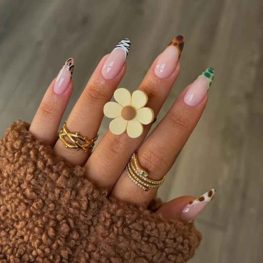Mixed animal-print French tips on pink almond nails, including zebra, leopard, tortoiseshell, and green croc.
