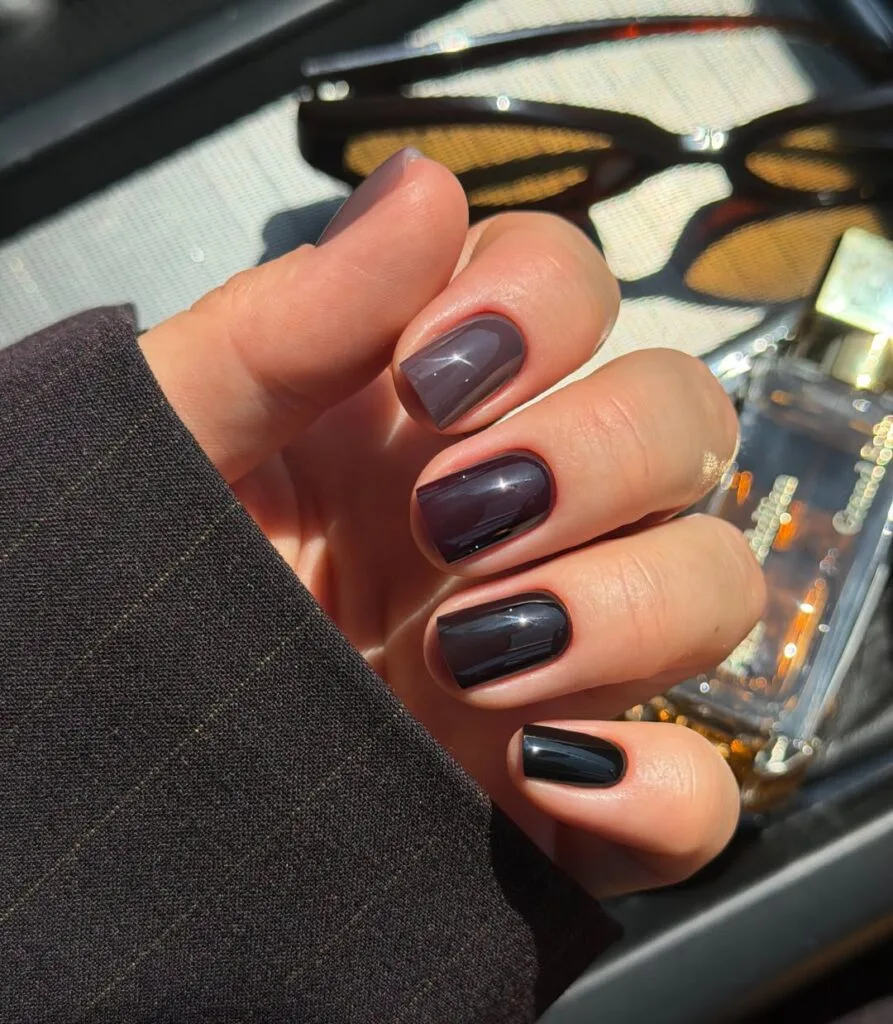 Short square nails in different glossy shades of grayish taupe, plum, charcoal, and black.