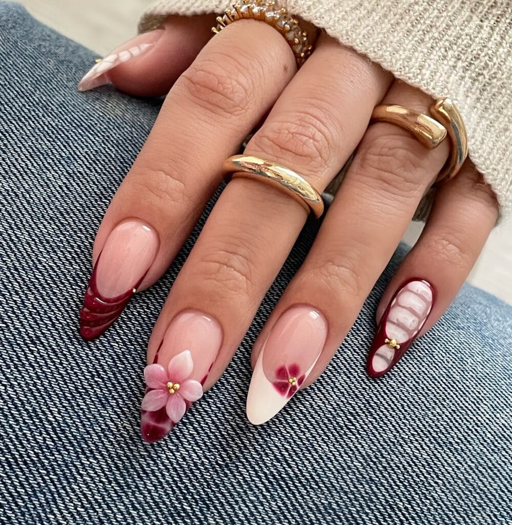 Pointed autumn nails with burgundy and cream French tips, a pink 3D flower, raised details, and gold beads.
