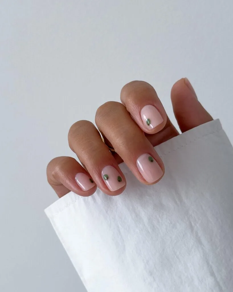 Short square pale pink nails with tiny green olive designs and reddish-brown centers.