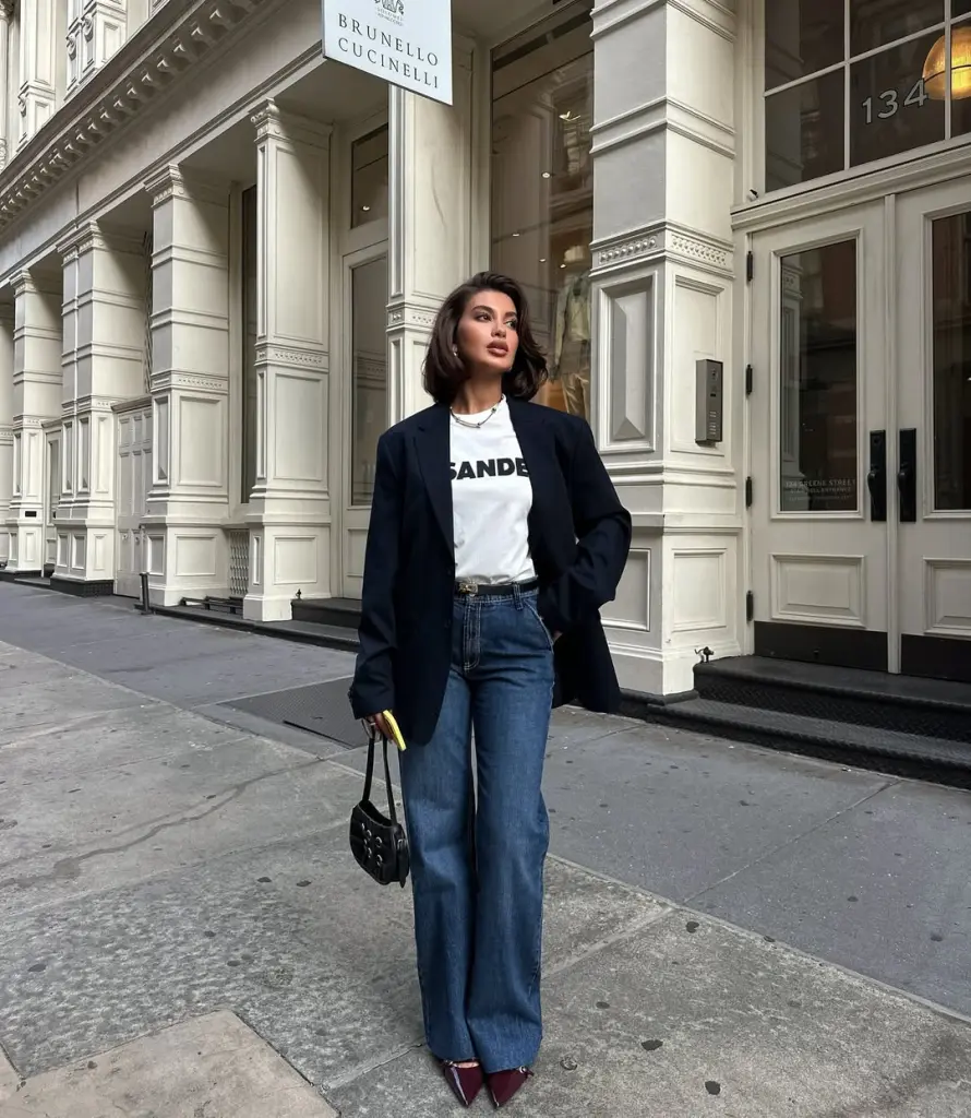 Classy fall outfit with navy oversized blazer, white graphic t-shirt, wide-leg jeans, burgundy pointed heels and black mini bag
