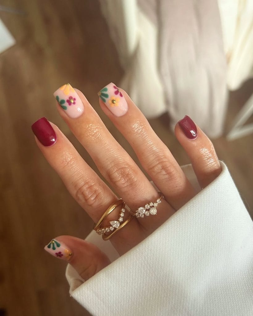 Mixed September nails with burgundy polish and floral designs on nude base