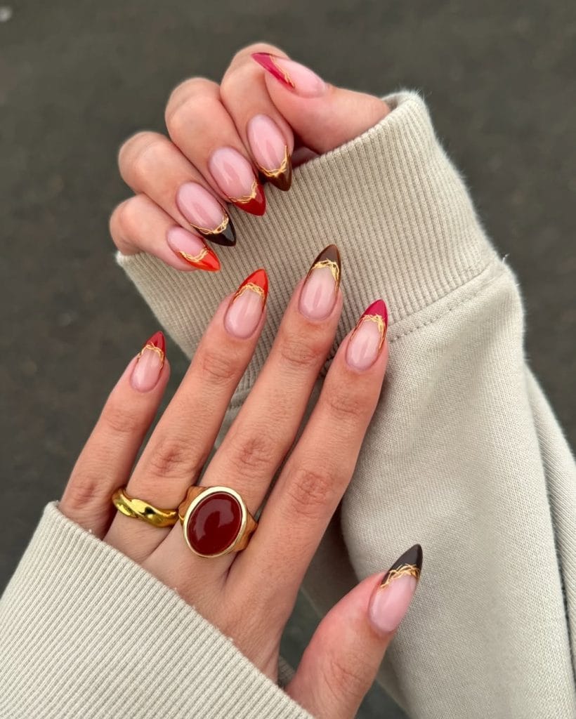 Colorful fall French tip nails with gold lines on pink base with red orange burgundy tips