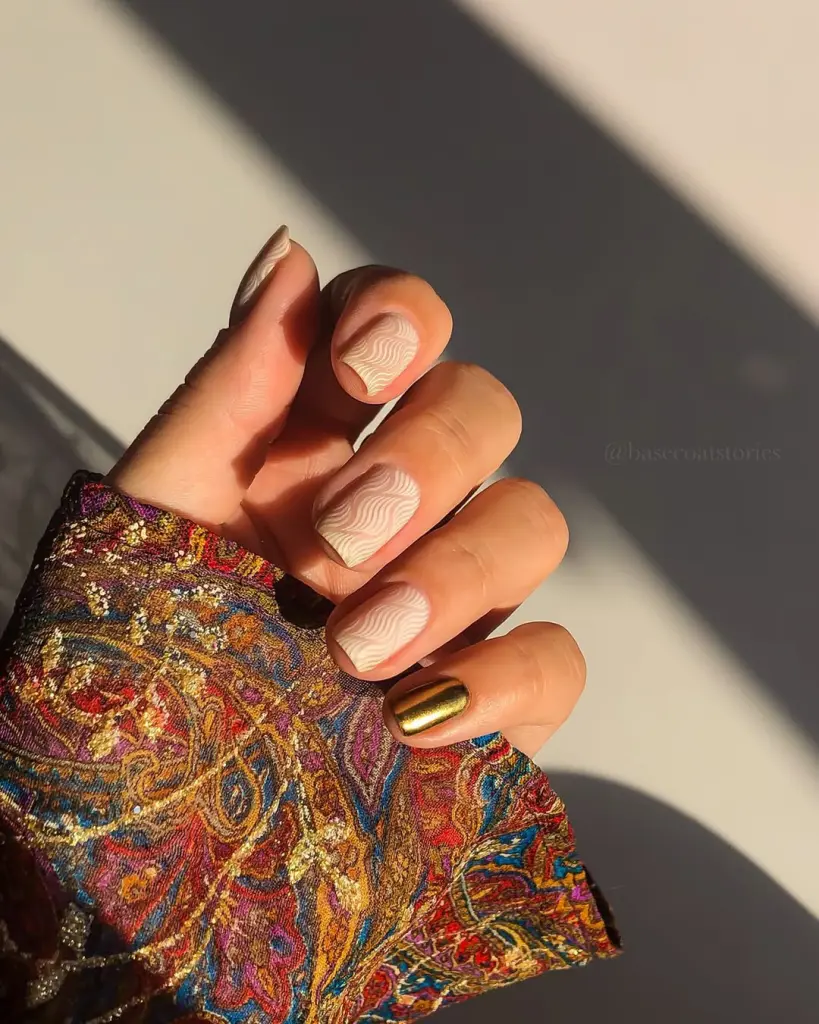 Fall short nails with nude base and white swirl patterns plus gold chrome accent nail