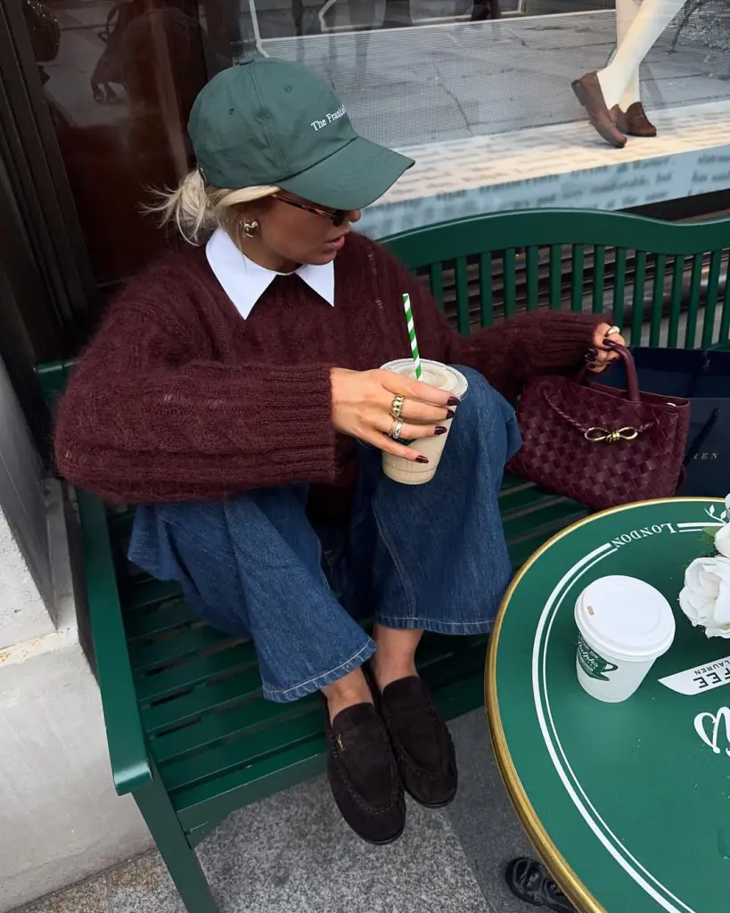 Fall outfit with burgundy knit sweater over white collared shirt, straight-leg jeans, green baseball cap and saude loafers