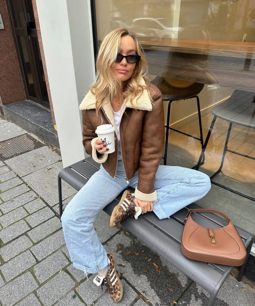 Casual fall outfit with brown shearling-lined jacket, white tee, light wash jeans, leopard print sneakers
