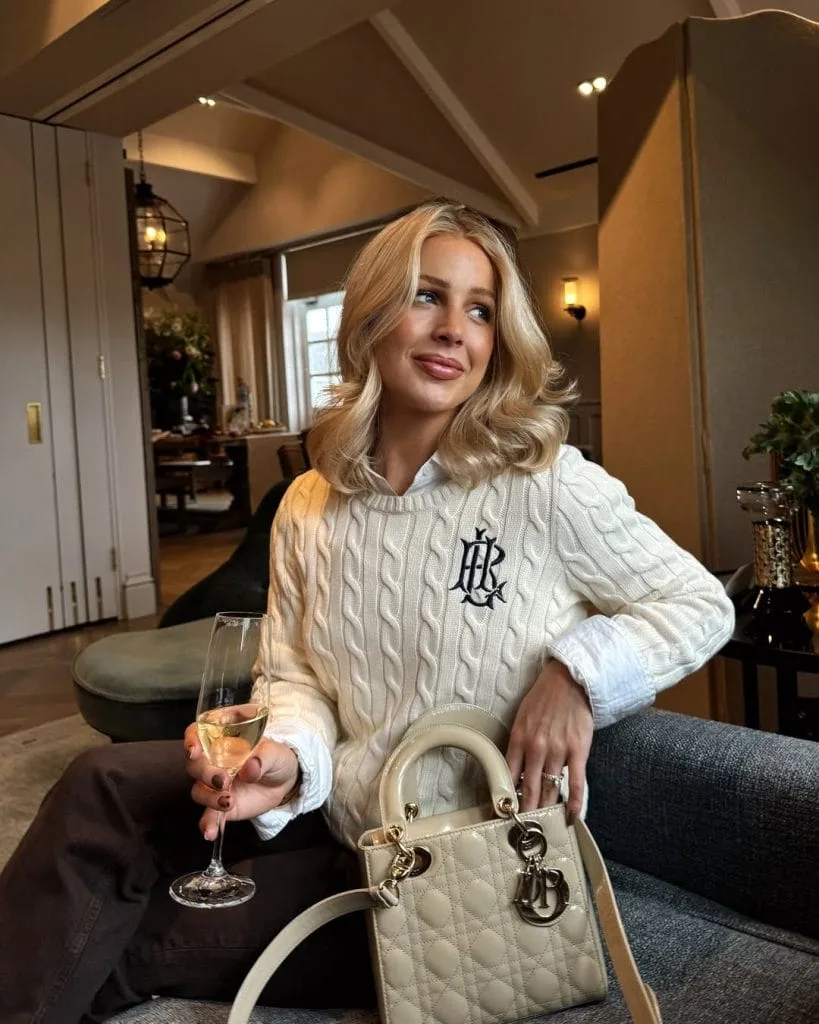 Preppy old money outfit with monogrammed cream cable knit sweater, white shirt and dark trousers