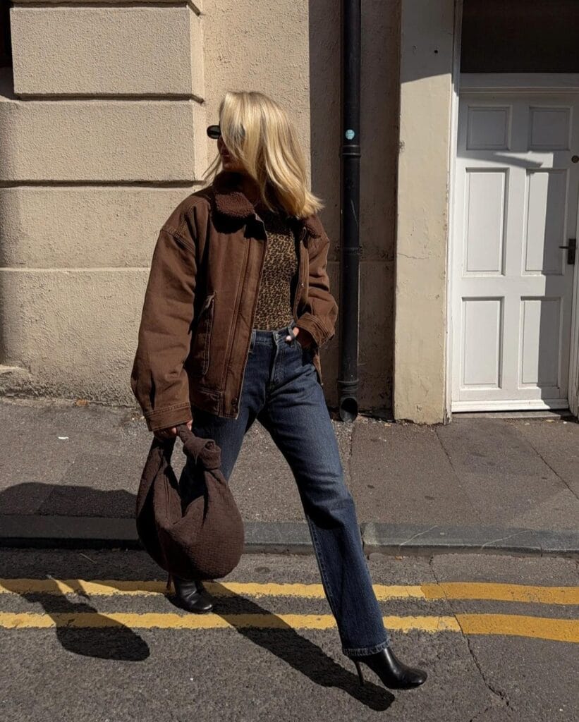 Casual autumn outfit with brown shearling-collar jacket, leopard print top, dark jeans, and black ankle boots