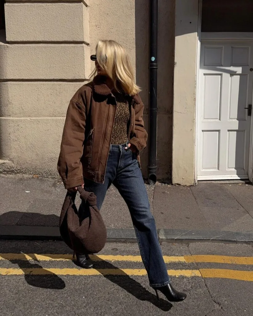 Casual autumn outfit with brown shearling-collar jacket, leopard print top, dark jeans, and black ankle boots
