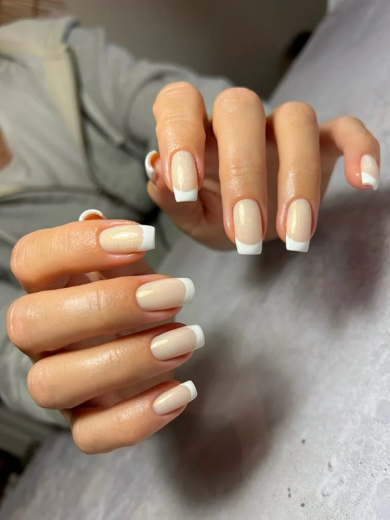 Square French manicure with gold shimmer in a nude base and crisp white tips.