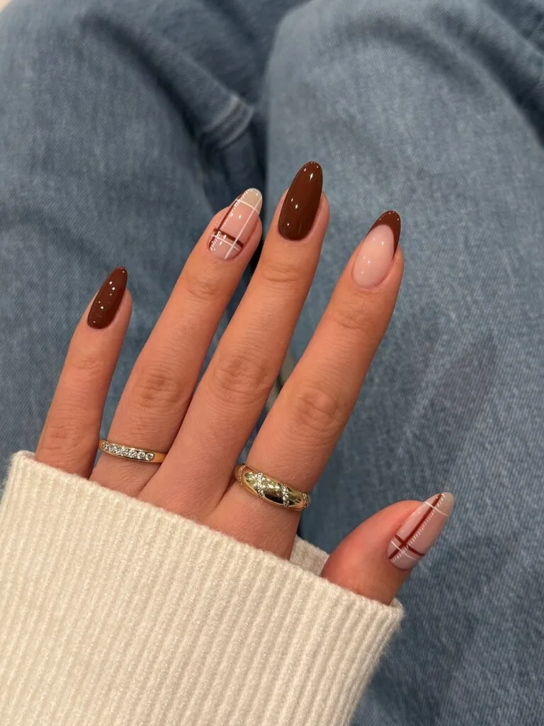 Almond brown fall nails with glossy chocolate polish, a brown French tip, and brown and white plaid accents
