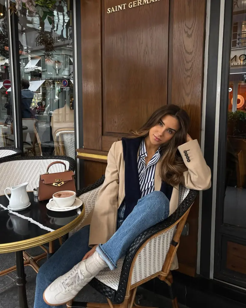 Chic fall outfit with beige oversized blazer, navy striped shirt, blue jeans, white chunky sneakers and brown structured handbag
