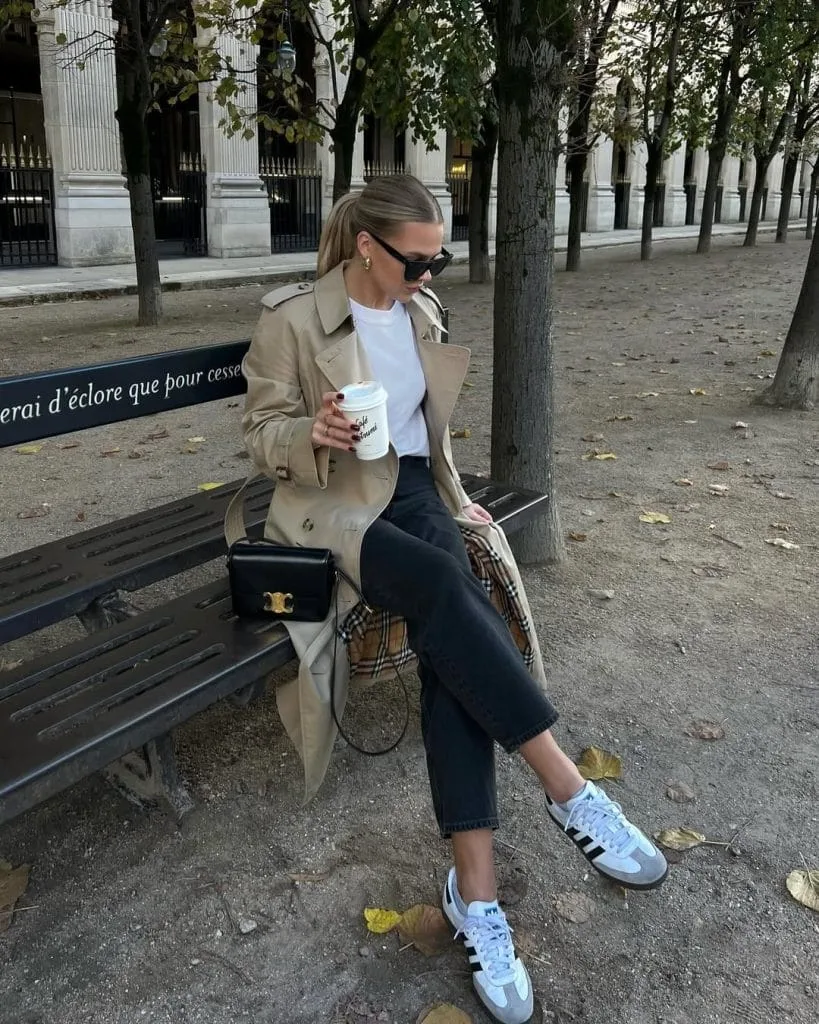 Casual fall outfit with beige trench coat, white t-shirt, black cropped jeans, light blue sneakers
