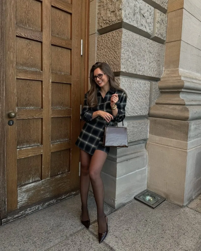 Classic old money outfit with dark plaid shirt dress, black tights and brown structured bag