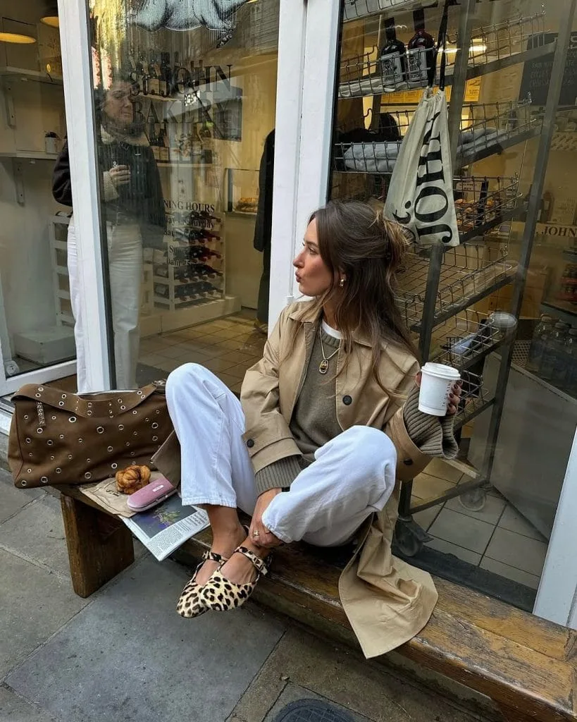 Casual fall outfit with beige trench coat, white jeans, leopard print mary janes, brown studded bag