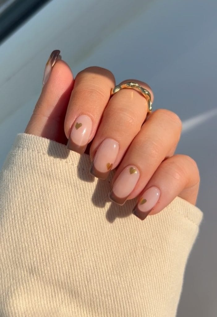 Gold brown fall French tip nails with matching gold heart accents on pink base