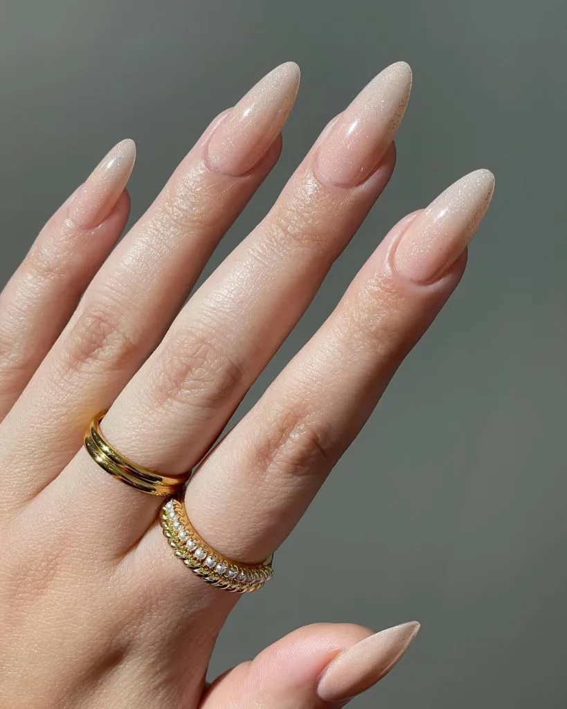 Long almond nude pink old money fall nails with shimmer finish and gold rings
