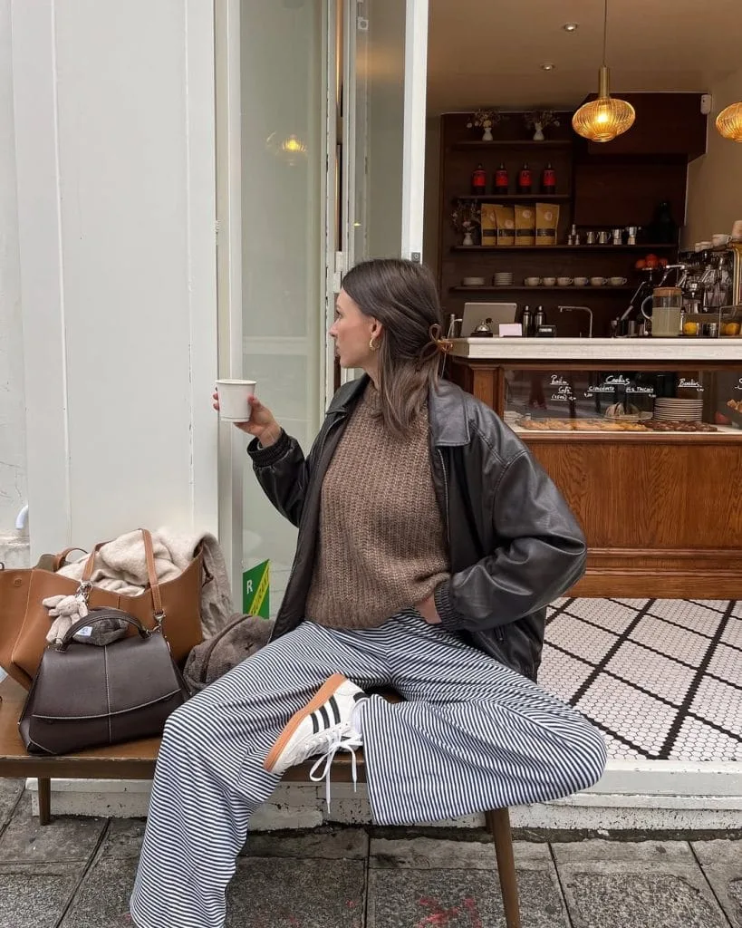Casual fall outfit with black leather jacket, taupe chunky sweater, black striped pants, white sneakers