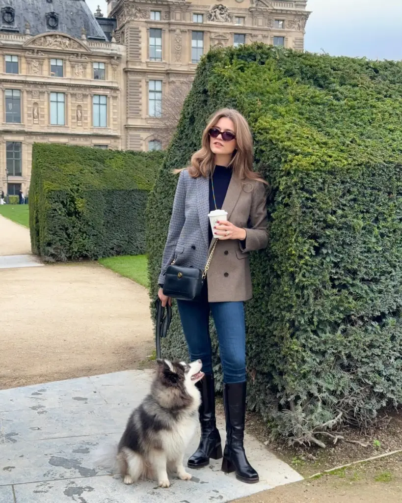 Effortless fall outfit with mixed pattern asymmetric blazer, navy top, fitted jeans, black knee-high boots and black crossbody bag
