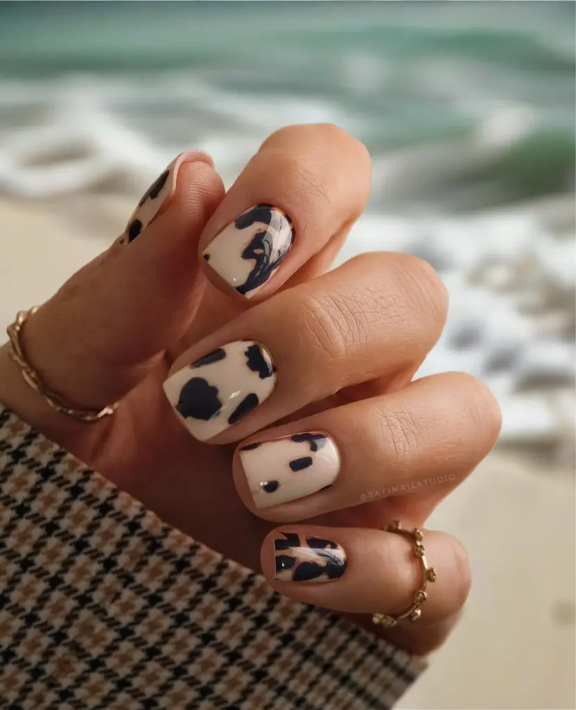 Short fall nails with black and cream cow print pattern design and glossy finish