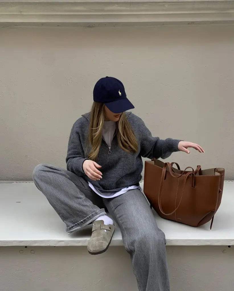 Comfy fall outfit with gray knit sweater, navy baseball cap, relaxed jeans and Birkenstocks with brown leather tote