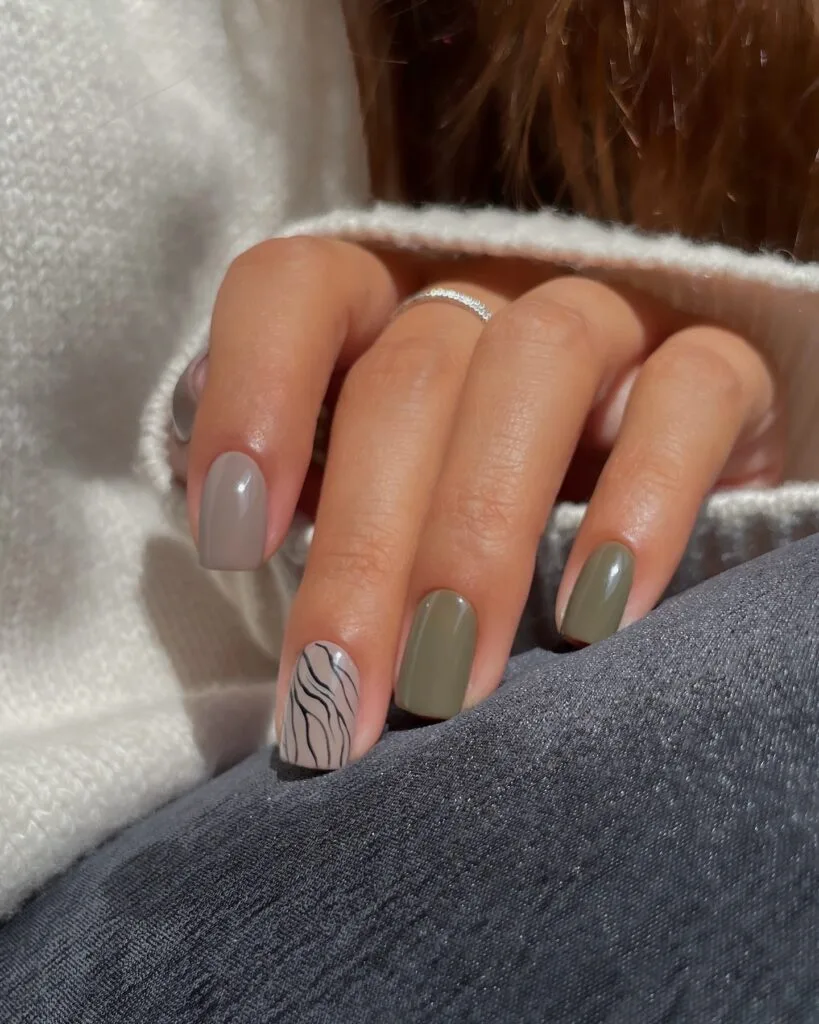 Short nail designs in muted olive and taupe with one black wavy line-art accent.
