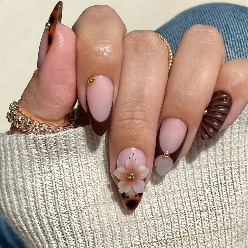 Autumn nails with pink bases, dark brown French tips, tortoiseshell tips, a 3D flower, gold beads, and a chocolate shell
