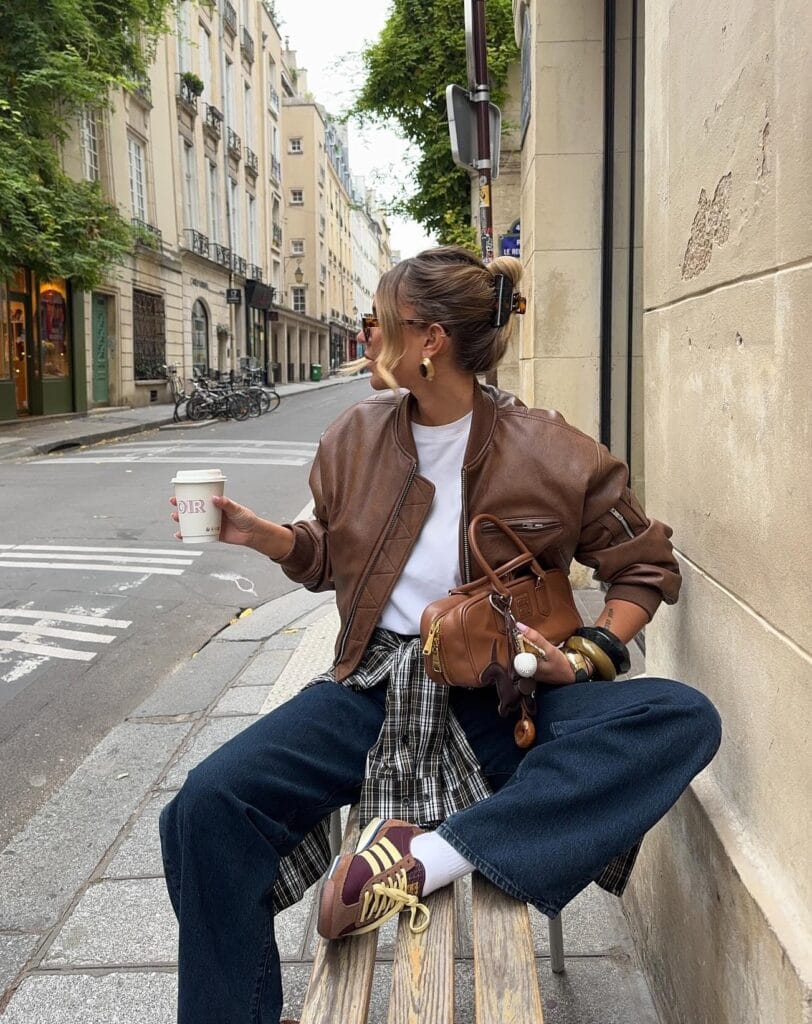 Everyday fall outfit with brown leather bomber, white tee, dark wide-leg jeans, and plaid shirt tied at the waist