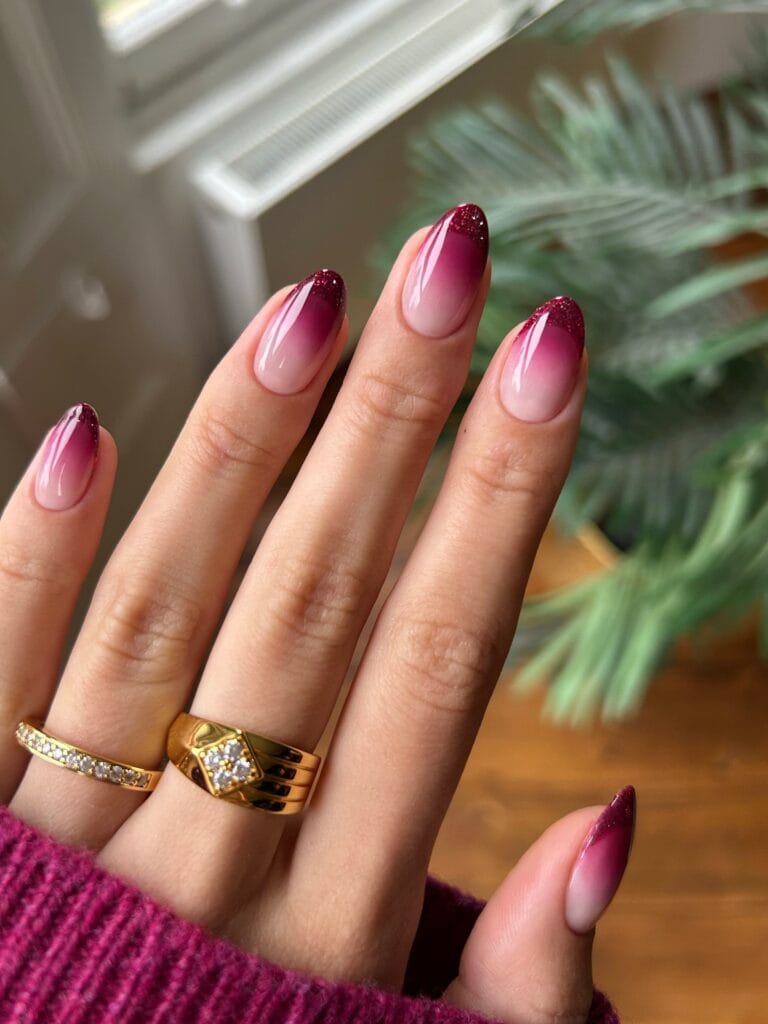 Almond autumn nails with deep berry ombré, pale pink bases, and fine glitter concentrated at the tips.