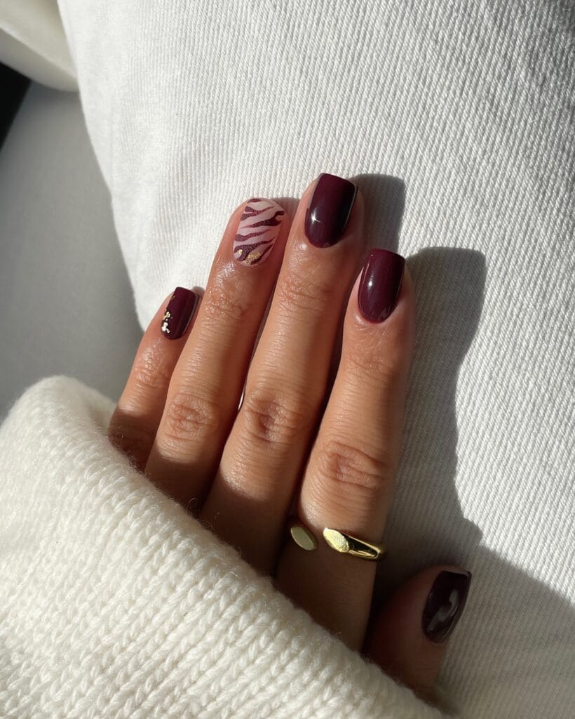 Classy burgundy fall nails with a pink zebra-striped accent and small gold foil details on short square tips.