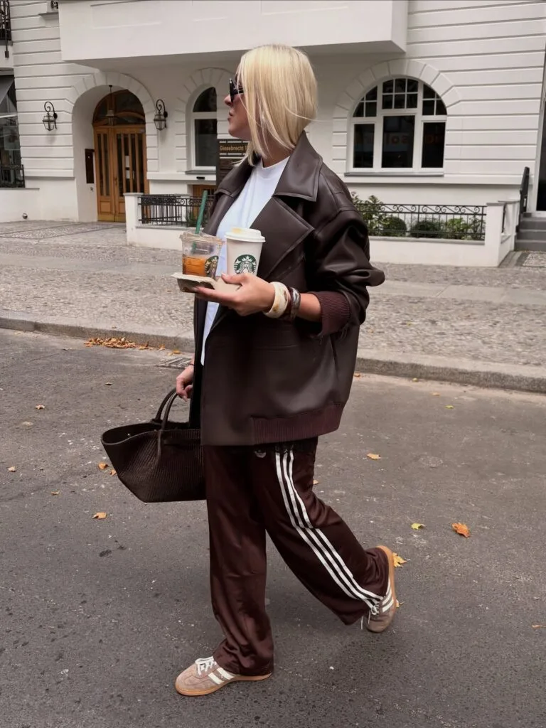 Casual fall outfit with oversized brown leather jacket, brown striped track pants, suede sneakers, and brown woven tote

