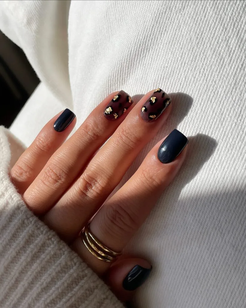 Short square fall nails in deep navy with burgundy-brown tortoiseshell accents and gold foil.
