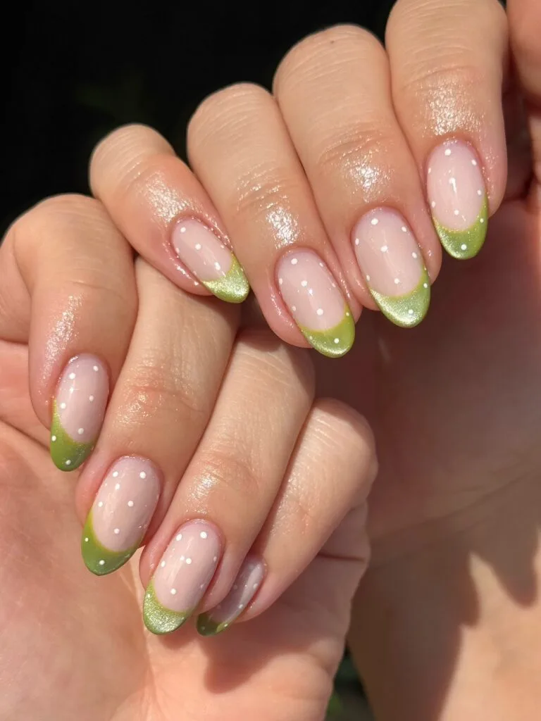 Rounded fall French tip nails with pink bases, shimmery green tips, and scattered white polka dots