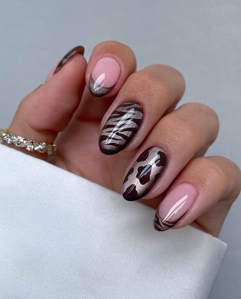 Brown fall nails with pink French tips, champagne cat-eye shimmer, zebra print, and cow print accents on almond nails