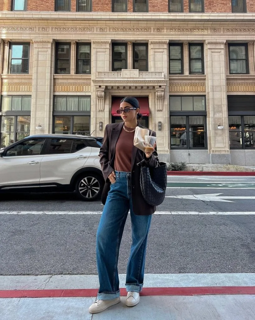Casual fall outfit with brown blazer, rust colored top, dark wash wide-leg jeans, white sneakers
