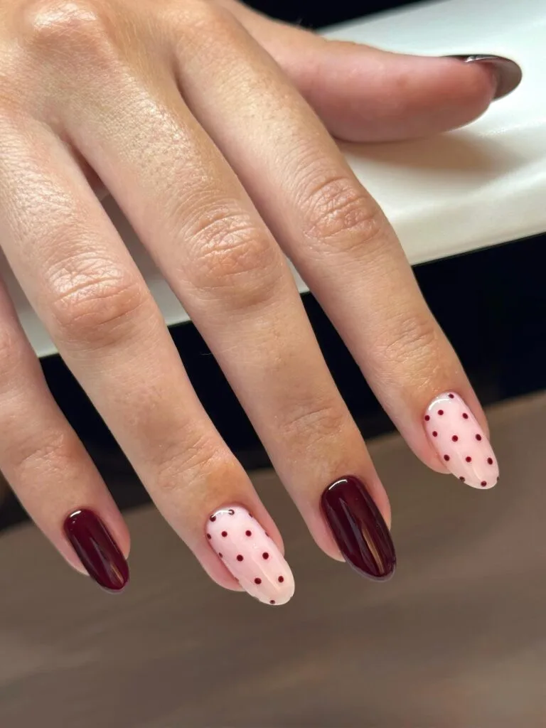 Simple fall nails with glossy burgundy nails and pale pink accent nails with burgundy polka dots.