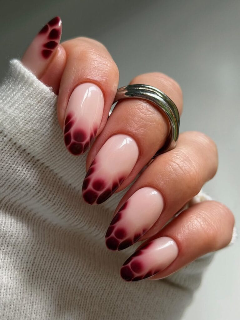 Almond autumn nails with nude pink bases and burgundy French tips formed by soft, reptile-like spots.