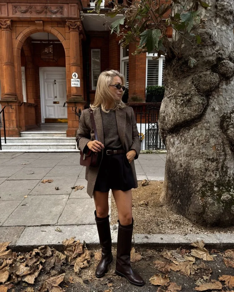 old money autumn outfit with brown herringbone blazer, black pleated mini skirt and tall brown boots