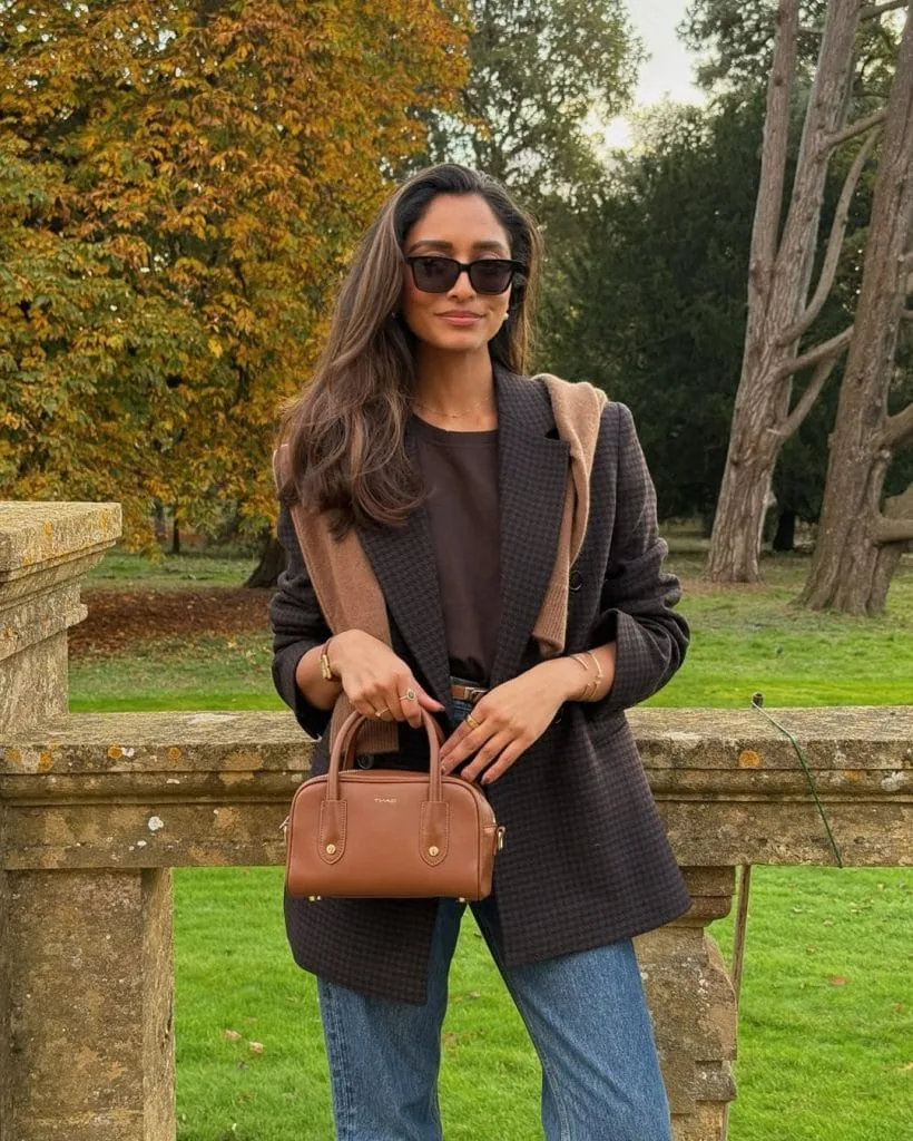Classic old money outfit with grey plaid blazer, brown sweater, straight jeans and cognac bag