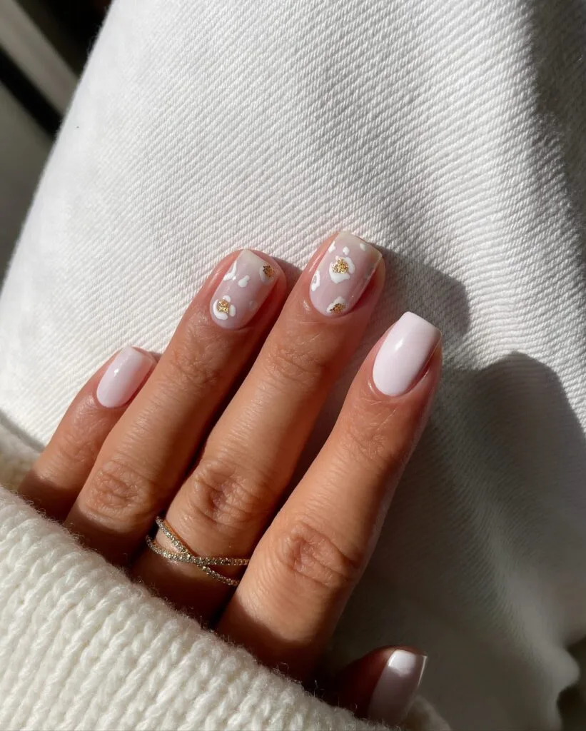 Short autumn nails with milky white polish, blush accents, white leopard spots, and gold foil.