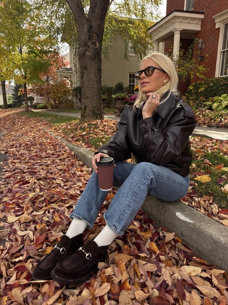 Casual fall outfit with dark brown leather bomber, cuffed light wash jeans, white socks, and brown suede loafers