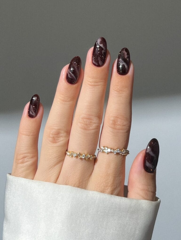 Black cherry brown fall nails with fine glitter and pale marble swirls on glossy almond nails