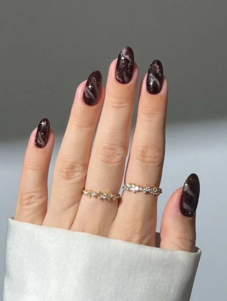 Black cherry brown fall nails with fine glitter and pale marble swirls on glossy almond nails
