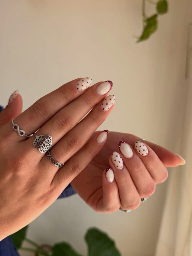 Autumn nails with creamy white bases, burgundy polka dots, and burgundy dotted French tips.